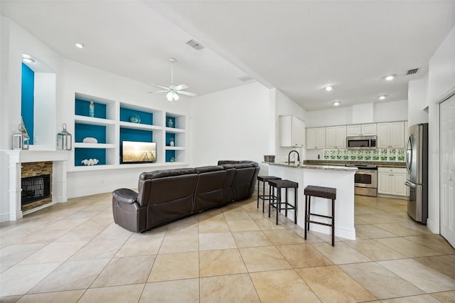 living room with ceiling fan, a fireplace, built in shelves, light tile patterned floors, and sink