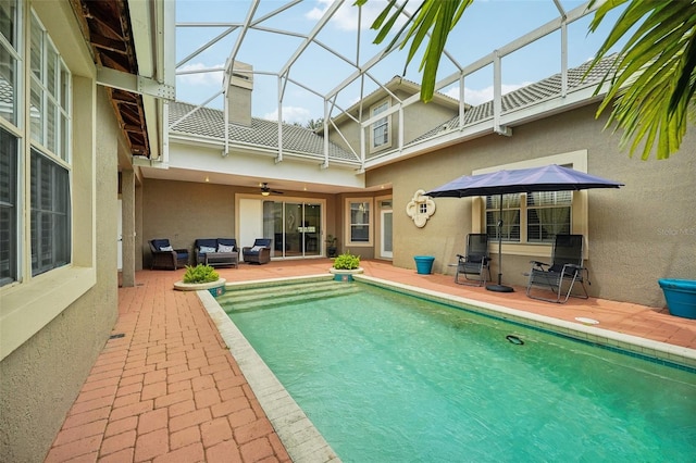 view of swimming pool featuring glass enclosure, ceiling fan, a patio area, and an outdoor living space