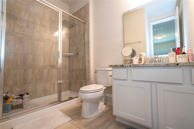 bathroom with vanity, a shower with door, toilet, and tile patterned floors