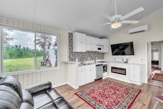 kitchen with light hardwood / wood-style flooring, a wall mounted AC, lofted ceiling, white cabinetry, and ceiling fan