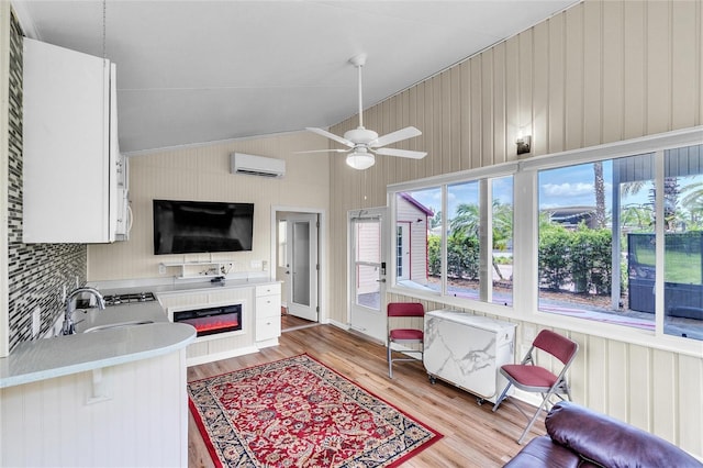 kitchen featuring white cabinets, vaulted ceiling, light wood-type flooring, an AC wall unit, and ceiling fan