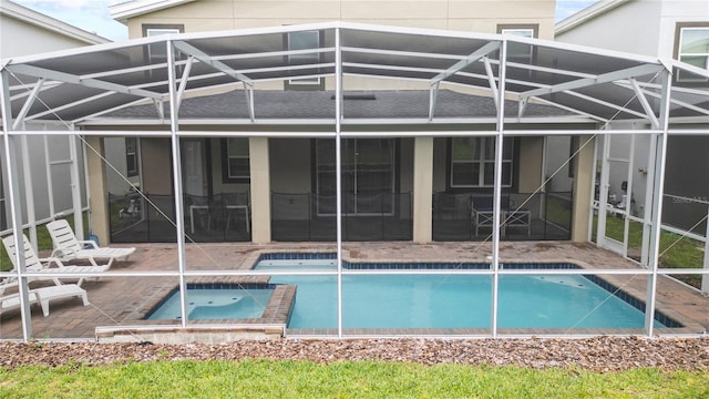 back of property featuring a swimming pool with hot tub, a patio, and glass enclosure