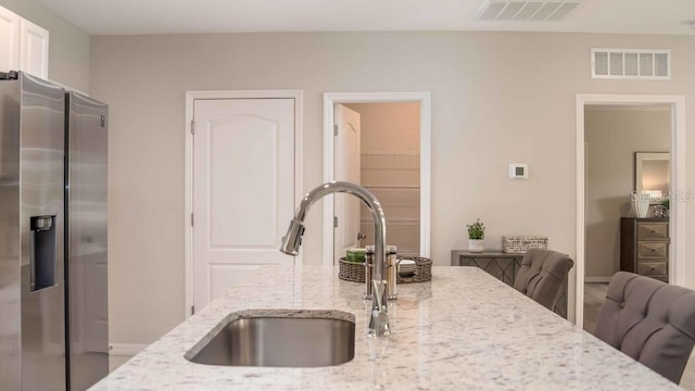 kitchen with sink, light stone counters, a kitchen breakfast bar, and stainless steel refrigerator with ice dispenser