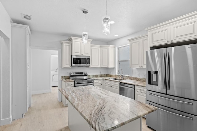 kitchen with stainless steel appliances, hanging light fixtures, light wood-type flooring, sink, and washer / clothes dryer