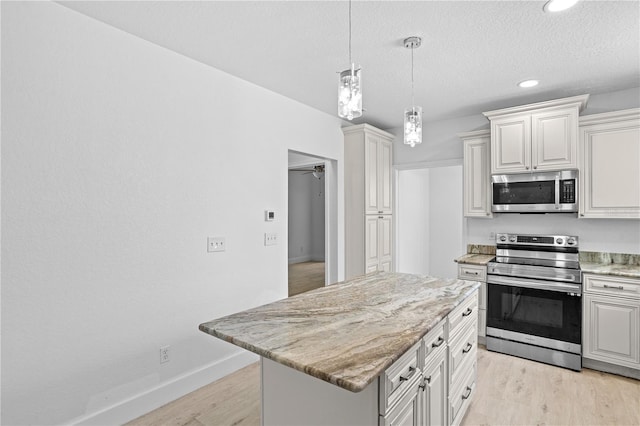 kitchen with stainless steel appliances, pendant lighting, light stone counters, a kitchen island, and light hardwood / wood-style floors