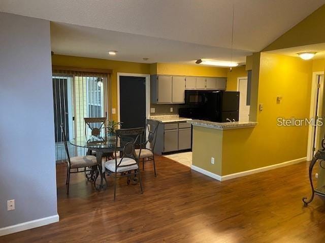 kitchen featuring baseboards, wood finished floors, freestanding refrigerator, a peninsula, and light countertops