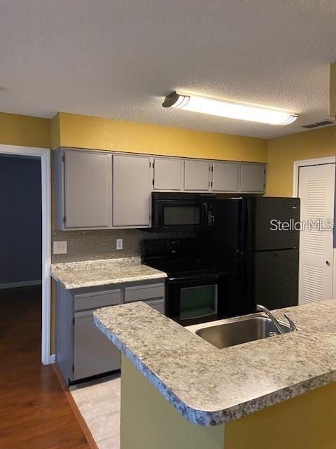 kitchen with black appliances, a sink, light countertops, and gray cabinetry