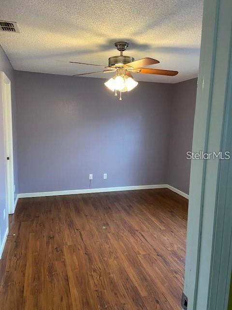 empty room with ceiling fan, dark wood-style flooring, visible vents, and baseboards