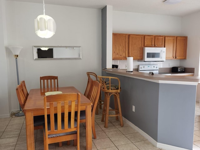 kitchen featuring light tile patterned flooring, kitchen peninsula, white appliances, and decorative light fixtures