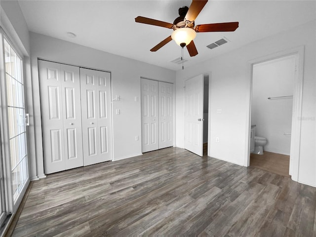 unfurnished bedroom featuring ceiling fan, ensuite bath, dark hardwood / wood-style flooring, and two closets