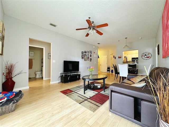 living room with ceiling fan, light hardwood / wood-style flooring, and a textured ceiling