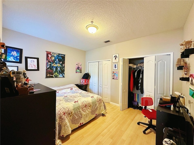 bedroom featuring two closets, a textured ceiling, and light wood-type flooring