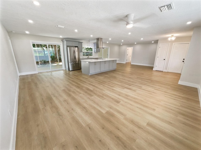 unfurnished living room with ceiling fan, a textured ceiling, and light wood-type flooring