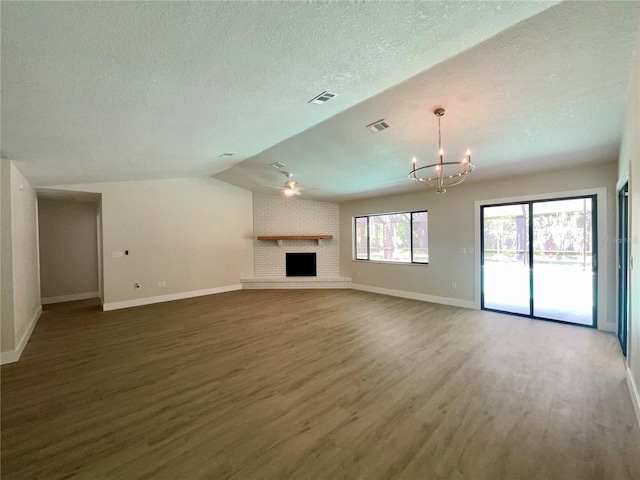 unfurnished living room featuring an inviting chandelier, dark hardwood / wood-style floors, a textured ceiling, a brick fireplace, and lofted ceiling