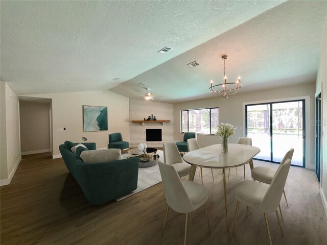 dining area featuring an inviting chandelier, a textured ceiling, a brick fireplace, lofted ceiling, and wood-type flooring