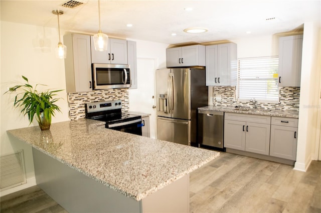 kitchen with kitchen peninsula, stainless steel appliances, decorative light fixtures, and light hardwood / wood-style floors