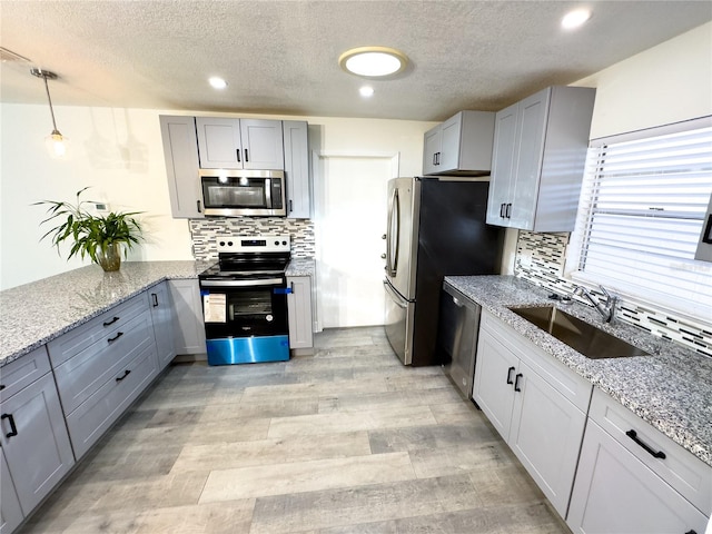 kitchen featuring light stone countertops, appliances with stainless steel finishes, tasteful backsplash, sink, and hanging light fixtures