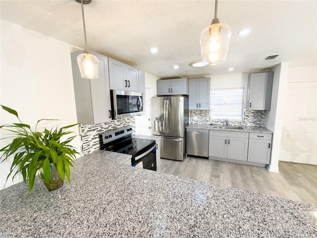 kitchen featuring appliances with stainless steel finishes, light hardwood / wood-style flooring, pendant lighting, and sink