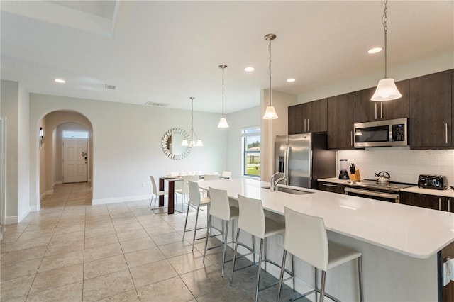 kitchen with backsplash, dark brown cabinetry, stainless steel appliances, and an island with sink