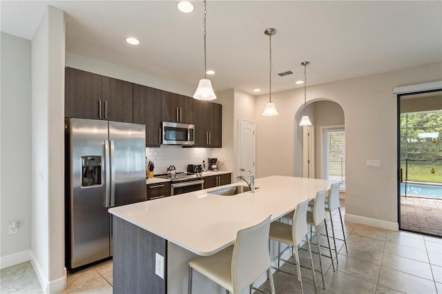 kitchen featuring decorative light fixtures, a center island with sink, a kitchen bar, sink, and appliances with stainless steel finishes