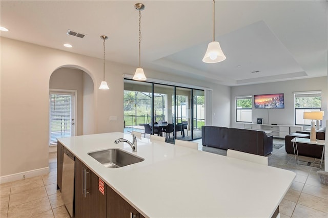 kitchen featuring a center island with sink, stainless steel dishwasher, sink, a tray ceiling, and light tile patterned floors