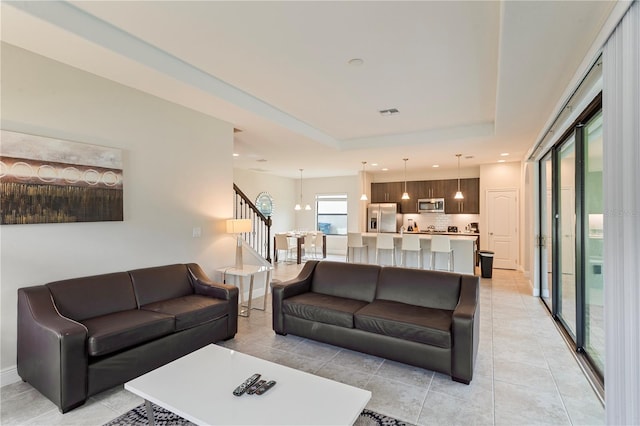 tiled living room with a tray ceiling and a chandelier