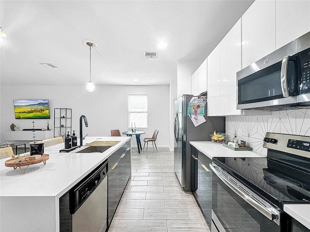 kitchen featuring appliances with stainless steel finishes, tasteful backsplash, sink, white cabinets, and hanging light fixtures