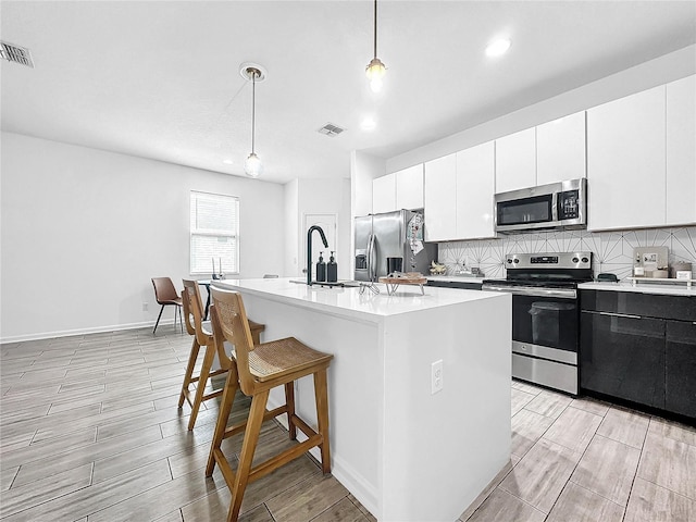 kitchen featuring a center island with sink, appliances with stainless steel finishes, pendant lighting, and white cabinets