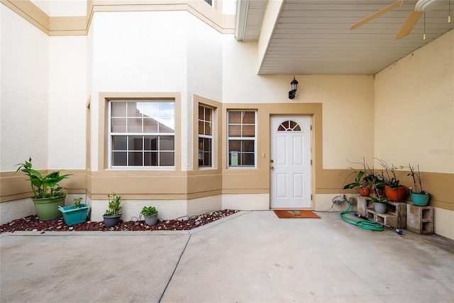 view of exterior entry with ceiling fan and a patio area