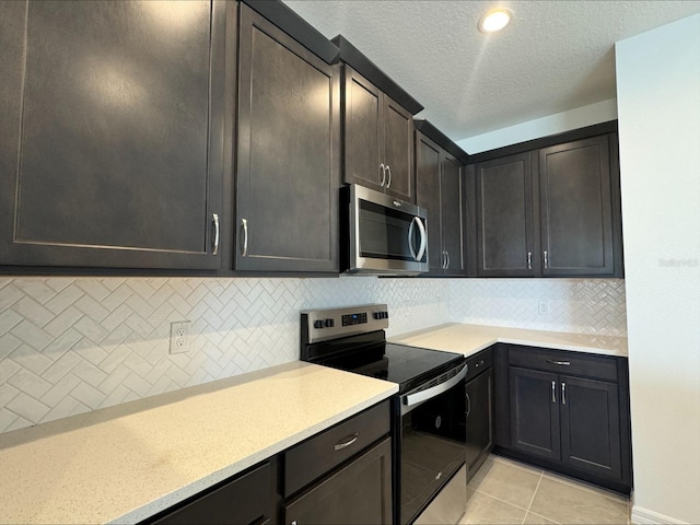 kitchen featuring decorative backsplash, light tile patterned floors, a textured ceiling, and appliances with stainless steel finishes