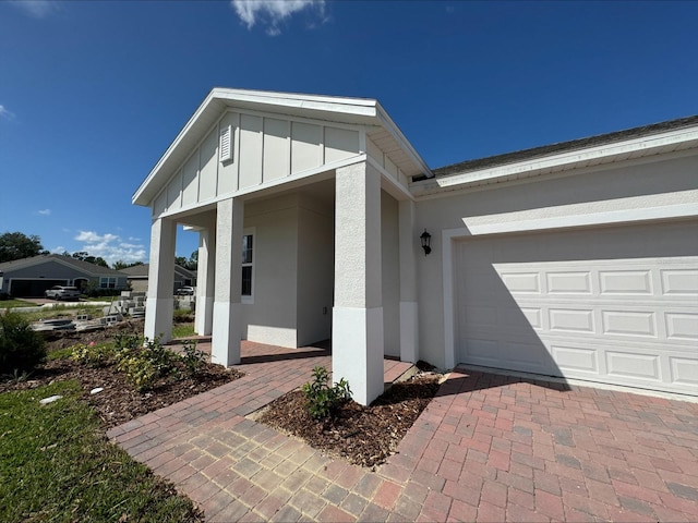 view of exterior entry featuring a garage, decorative driveway, board and batten siding, and stucco siding