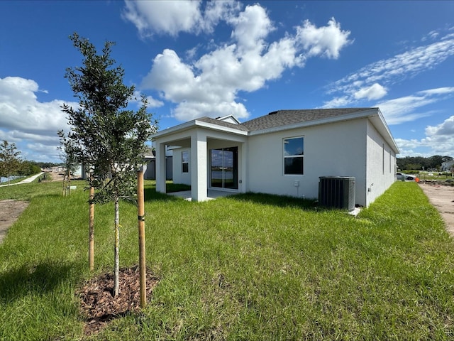 back of property with a yard, central AC unit, and stucco siding