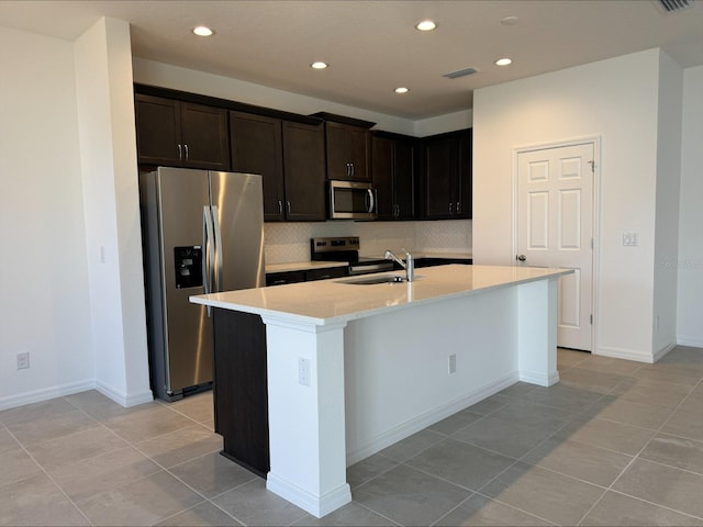 kitchen with sink, stainless steel appliances, tasteful backsplash, an island with sink, and light tile patterned floors