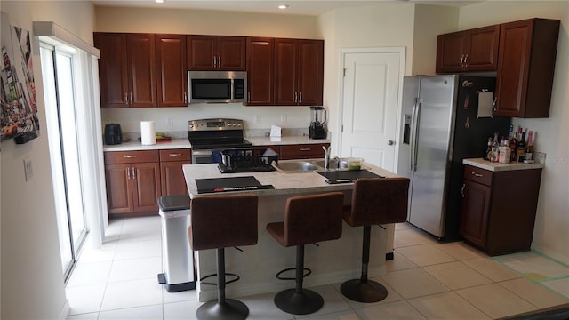 kitchen with sink, a breakfast bar area, light tile patterned floors, stainless steel appliances, and a kitchen island with sink