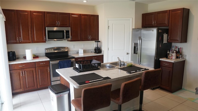 kitchen featuring light tile patterned floors, sink, a breakfast bar area, appliances with stainless steel finishes, and a center island with sink