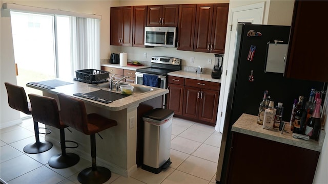 kitchen with a kitchen island with sink, stainless steel appliances, a kitchen breakfast bar, and light tile patterned flooring