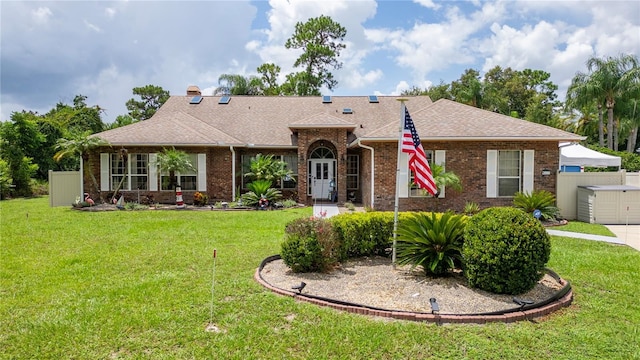 single story home with a shingled roof, a front lawn, and brick siding