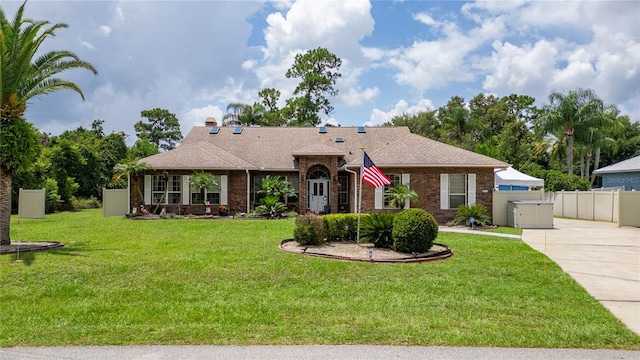 ranch-style house with driveway, brick siding, roof with shingles, fence, and a front yard