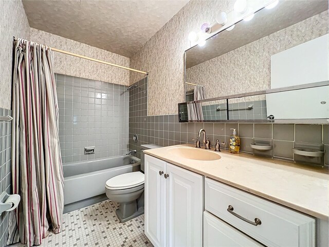 full bathroom with tile walls, vanity, toilet, shower / bathtub combination with curtain, and a textured ceiling