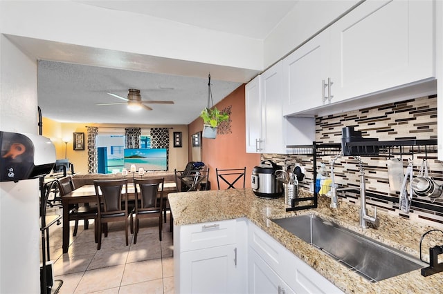 kitchen with white cabinetry, light tile patterned floors, backsplash, light stone counters, and ceiling fan