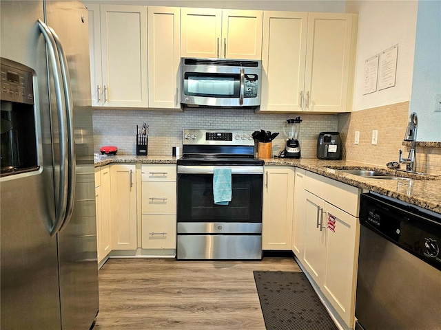 kitchen featuring tasteful backsplash, stainless steel appliances, sink, light stone counters, and light hardwood / wood-style floors