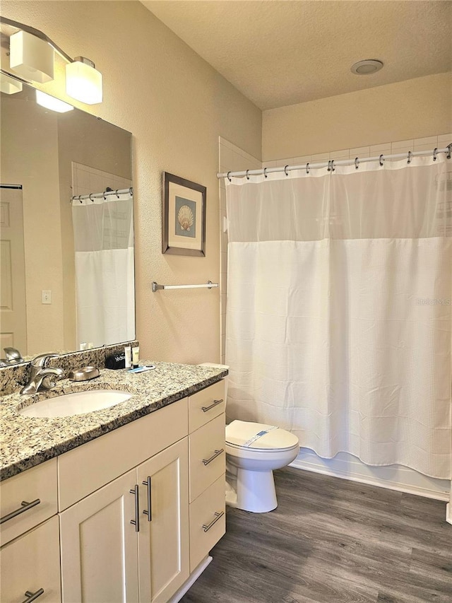 full bathroom with shower / tub combo with curtain, wood-type flooring, toilet, and vanity