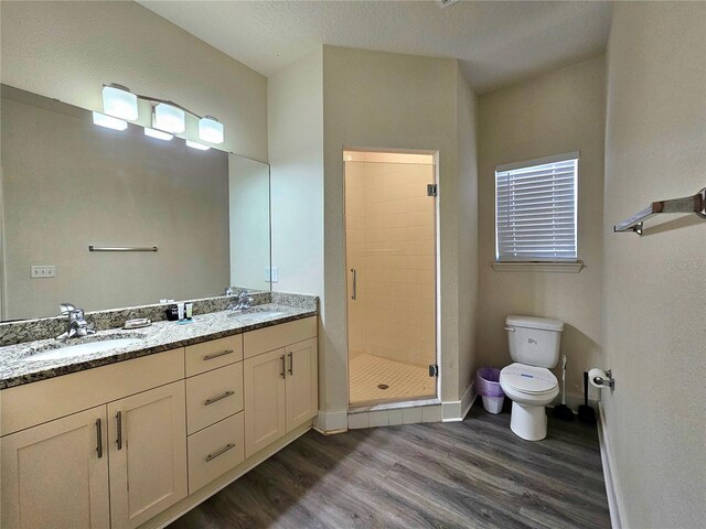 bathroom featuring double vanity, a shower with door, hardwood / wood-style floors, and toilet