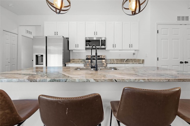 kitchen featuring white cabinets, a kitchen bar, stainless steel appliances, light stone countertops, and sink