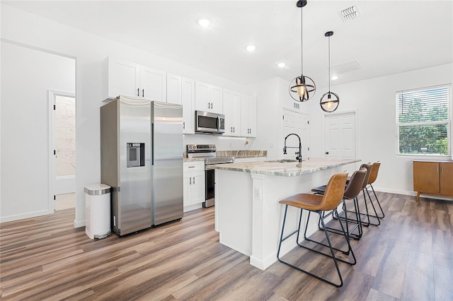 kitchen with white cabinetry, light wood-type flooring, stainless steel appliances, and a center island with sink