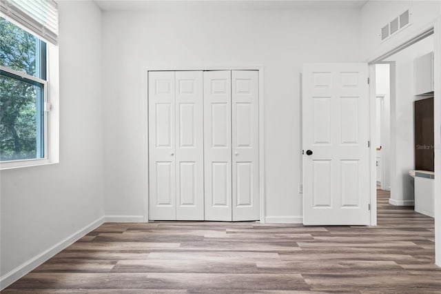 unfurnished bedroom with multiple windows, a closet, and hardwood / wood-style floors