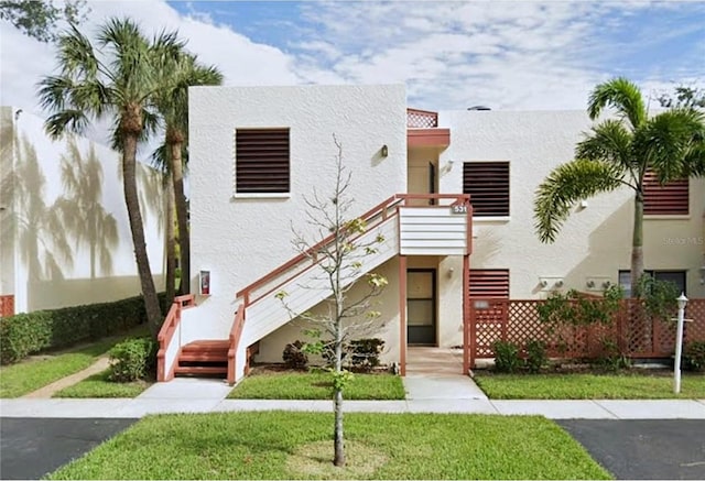 view of property with stucco siding, stairs, and a front yard