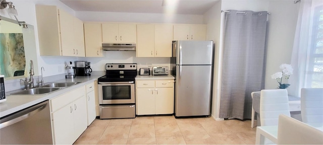 kitchen with appliances with stainless steel finishes, light tile patterned flooring, cream cabinetry, and sink