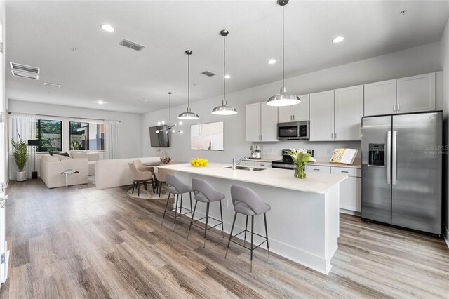 kitchen with stainless steel appliances, a breakfast bar area, light wood-type flooring, a center island with sink, and sink