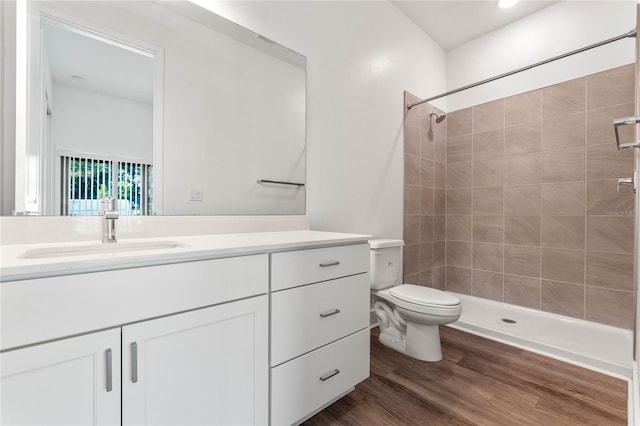 bathroom with hardwood / wood-style flooring, vanity, a tile shower, and toilet